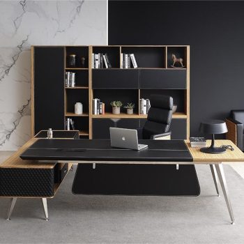 "A modern L-shaped executive desk with an inlaid black leather writing surface, zebrawood accents, silver metal legs, and a diamond-quilted side cabinet return."