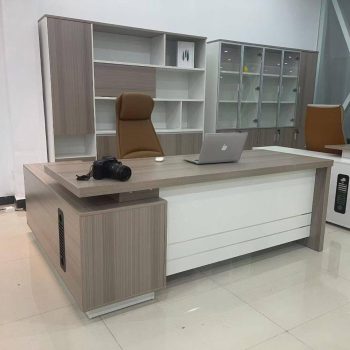 "A contemporary L-shaped executive desk featuring a light grey oak veneer finish, a floating-style desktop, and a stark white front modesty panel."