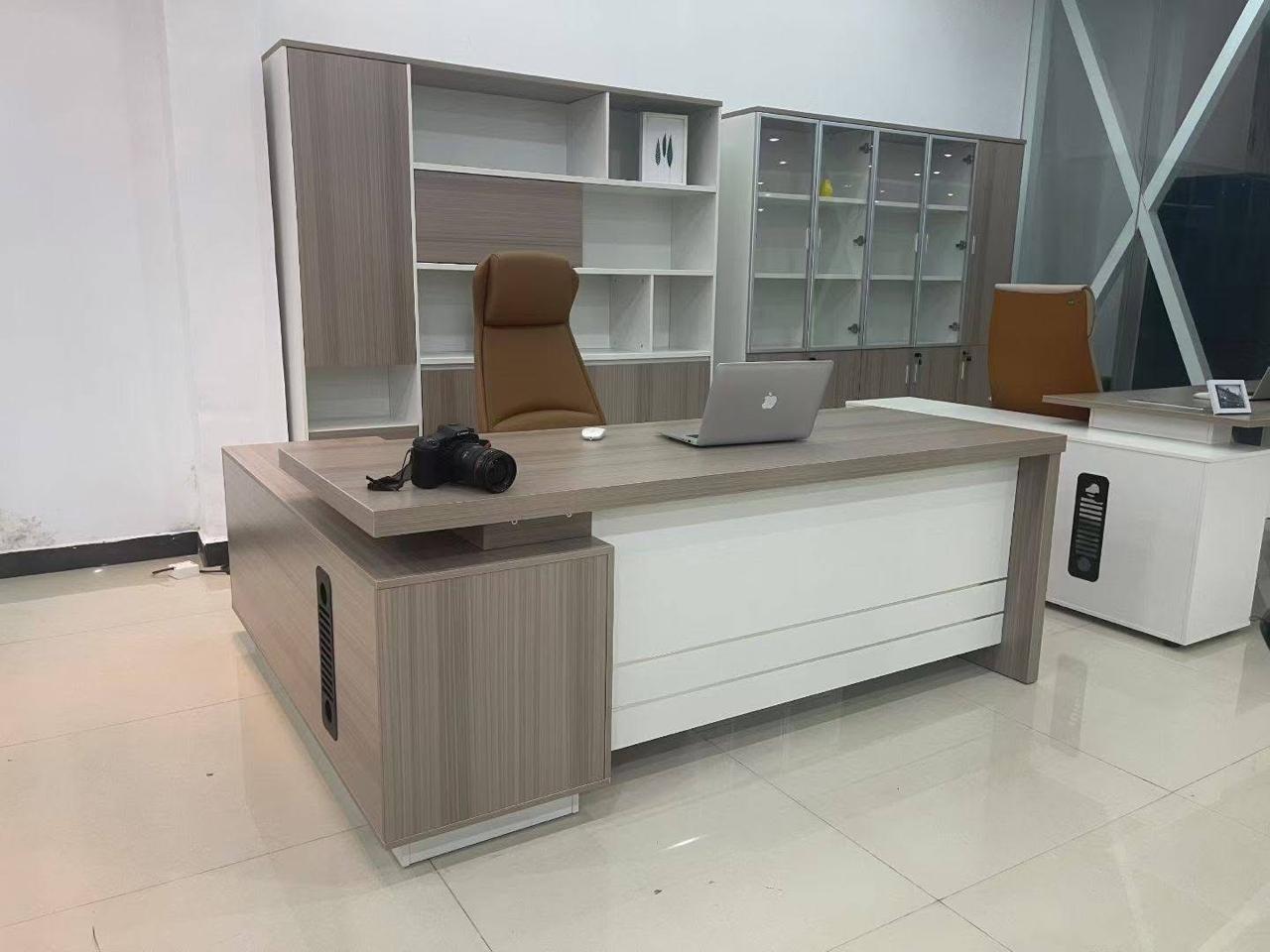 "A contemporary L-shaped executive desk featuring a light grey oak veneer finish, a floating-style desktop, and a stark white front modesty panel."