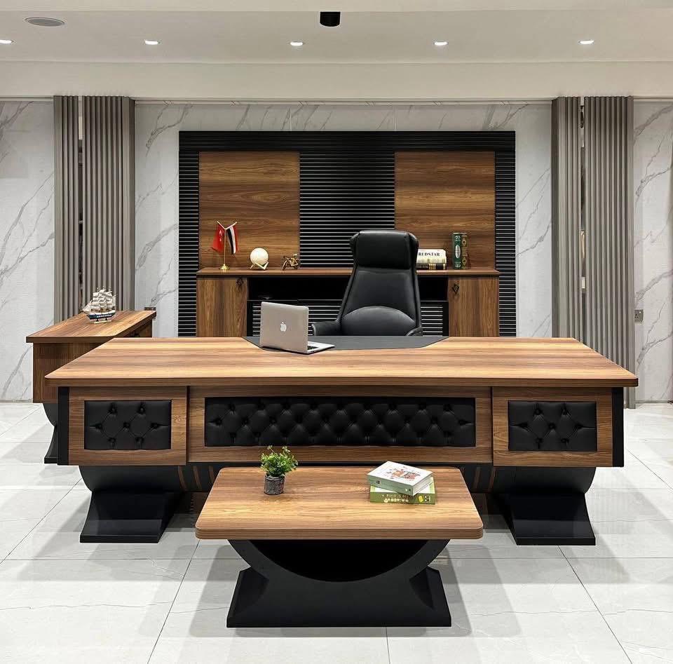 "A luxurious walnut wood executive desk featuring tufted black leather accents on the front modesty panel and heavy, curved black pedestal bases."