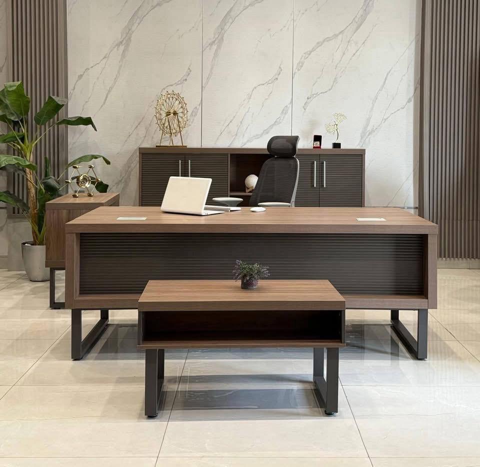 "A contemporary medium wood executive desk featuring a dark grey, horizontally slatted modesty panel and angled metal legs."