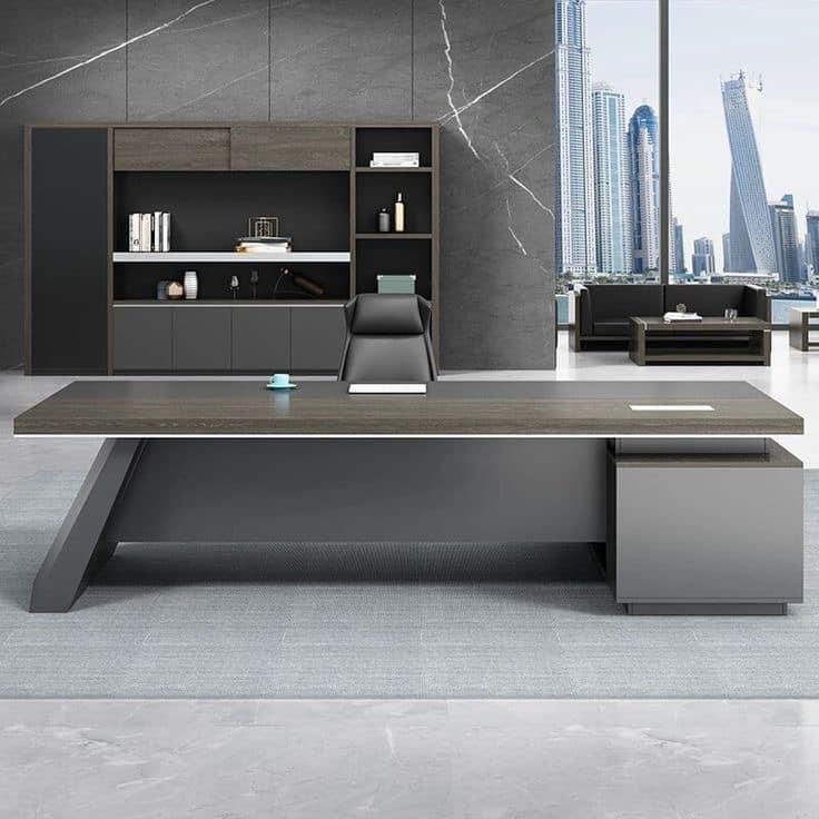 "A modern L-shaped executive desk in dark grey and grey oak wood veneer, featuring an angled leg base and a blocky side storage pedestal."