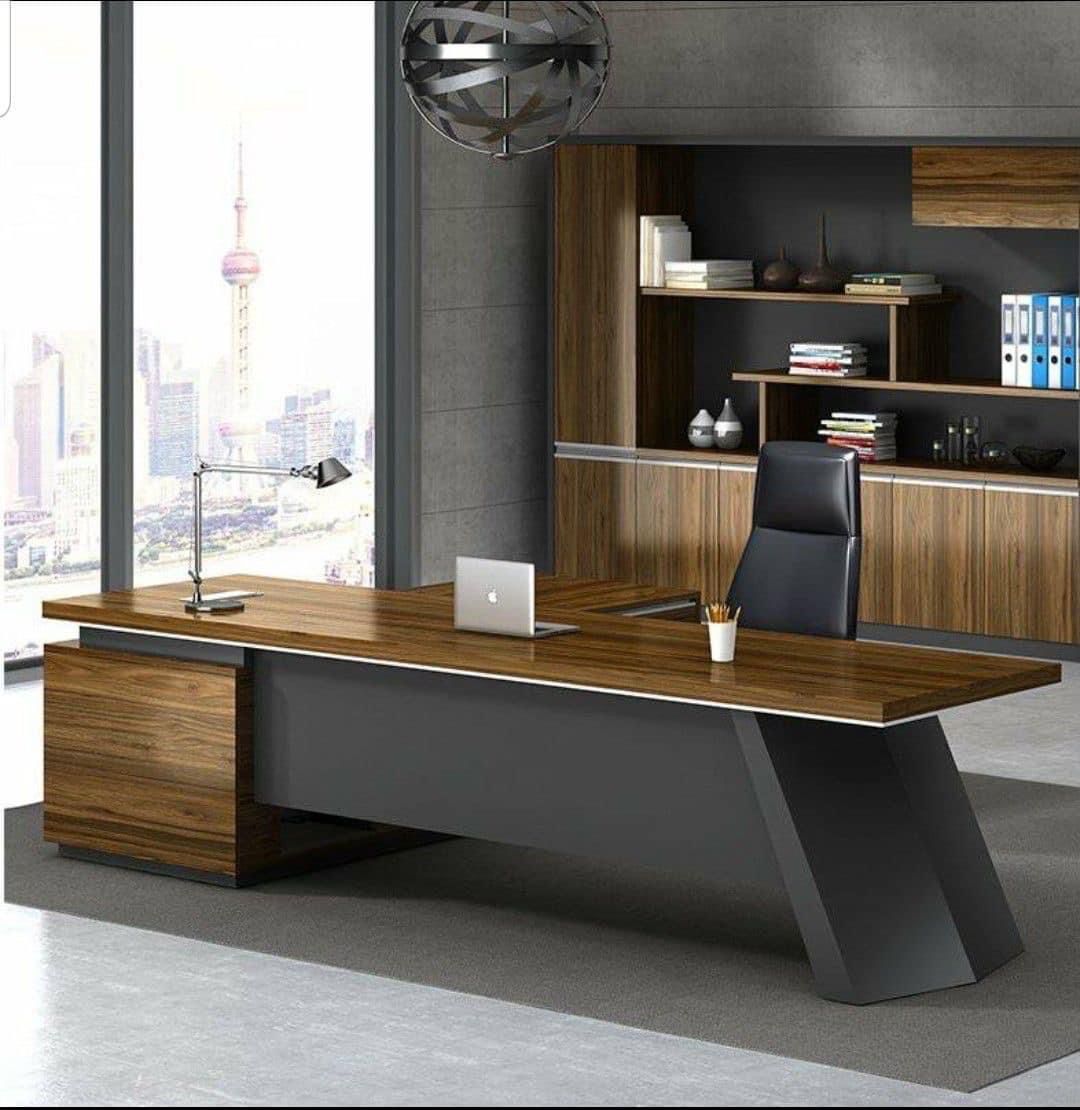 "A modern L-shaped executive desk featuring a rich walnut wood floating desktop, a matte dark grey modesty panel, and a bold, angled slab leg."