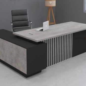 "A modern L-shaped executive desk in light grey wood and matte black, featuring a slatted vertical-line modesty panel and a low-profile side return."