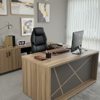 "An executive L-shaped manager desk in a light oak finish, featuring a charcoal grey front modesty panel detailed with intersecting geometric wood line accents."