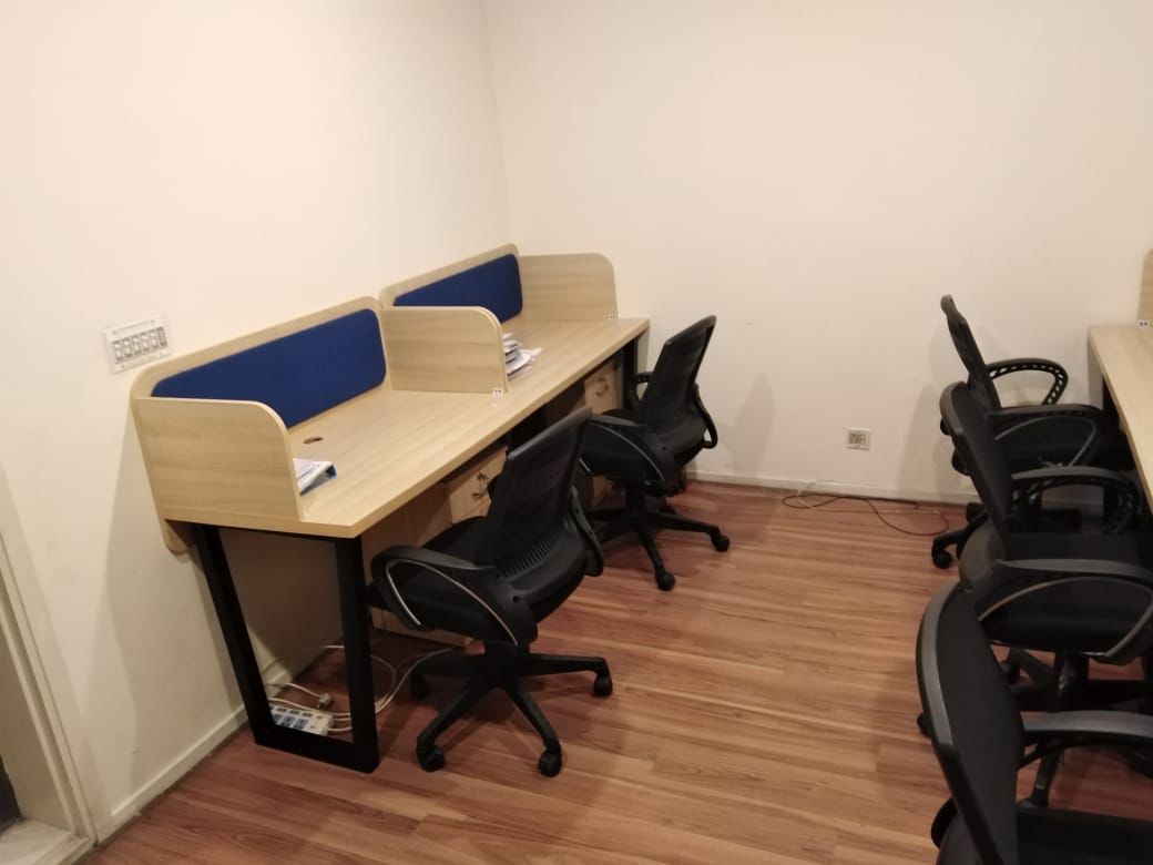 "A row of linear modular office cubicle desks featuring a light wood-grain laminate finish, integrated curved side privacy panels with blue fabric backboards, black metal legs, and built-in under-desk drawer units."