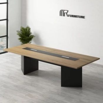 "A modern rectangular conference desk featuring a natural oak wood-grain top with a long black center media track and two thick, black angled slab pedestal bases."