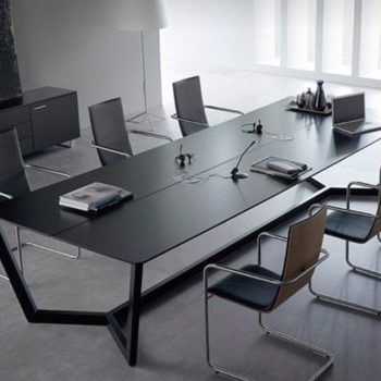 "A long, ultra-slim black rectangular executive conference desk featuring a minimalist matte finish and a sculptural, geometric black metal open-frame base."