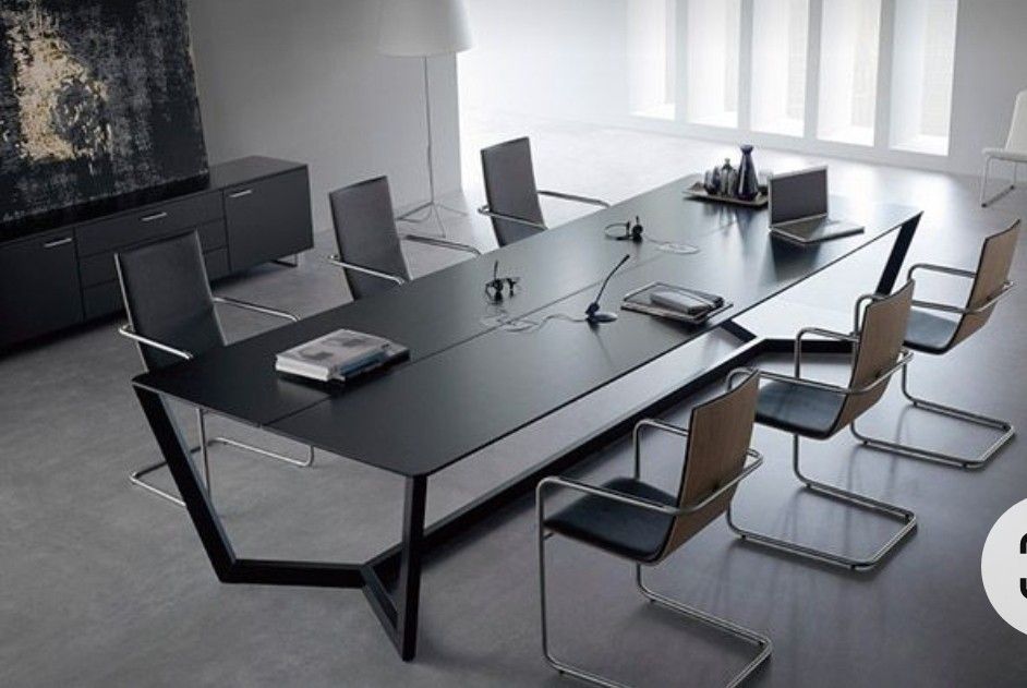 "A long, ultra-slim black rectangular executive conference desk featuring a minimalist matte finish and a sculptural, geometric black metal open-frame base."