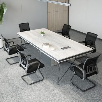 "A rectangular executive conference desk featuring a thick white-washed oak wood-grain top with a grey edge border, a central rectangular media port, supported by a grey box pedestal base and thin geometric wire-frame legs."