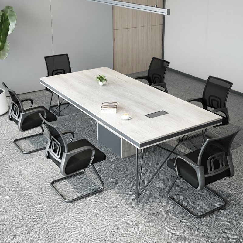 "A rectangular executive conference desk featuring a thick white-washed oak wood-grain top with a grey edge border, a central rectangular media port, supported by a grey box pedestal base and thin geometric wire-frame legs."