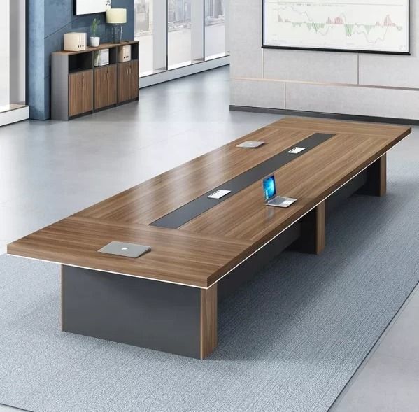 "A long, rectangular executive boardroom desk featuring a warm walnut wood-grain top with a recessed black center media track, supported by three thick charcoal-grey pedestal bases."
