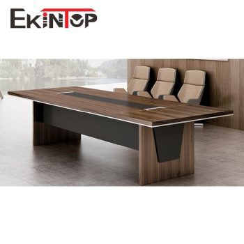 "A long, rectangular executive boardroom desk featuring a warm walnut wood-grain top with a black center media inlay track, supported by thick panel legs and a full-length black modesty panel."