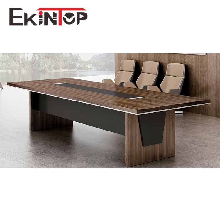 "A long, rectangular executive boardroom desk featuring a warm walnut wood-grain top with a black center media inlay track, supported by thick panel legs and a full-length black modesty panel."