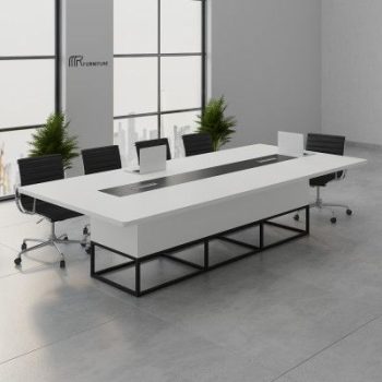 "A large, modern white conference room meeting table featuring a rounded rectangular tabletop with a long, recessed black center media track, a chunky white box-style base, and an open black metal geometric frame support."